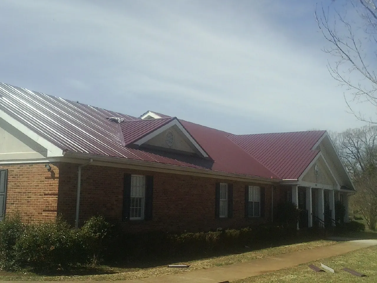 Red metal roof with gabled entries on a long brick building, from a Hail Damage Roof Repair job in Purcellville