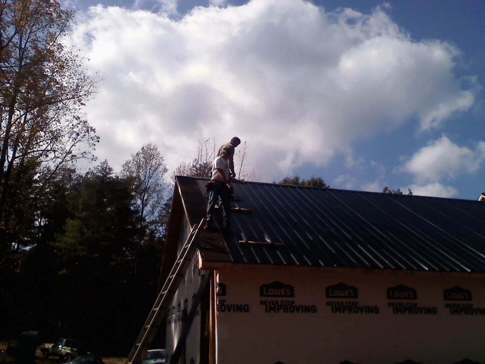 Roofer fastening dark metal panels high against a cloudy sky, from a Roof Inspection job in Purcellville