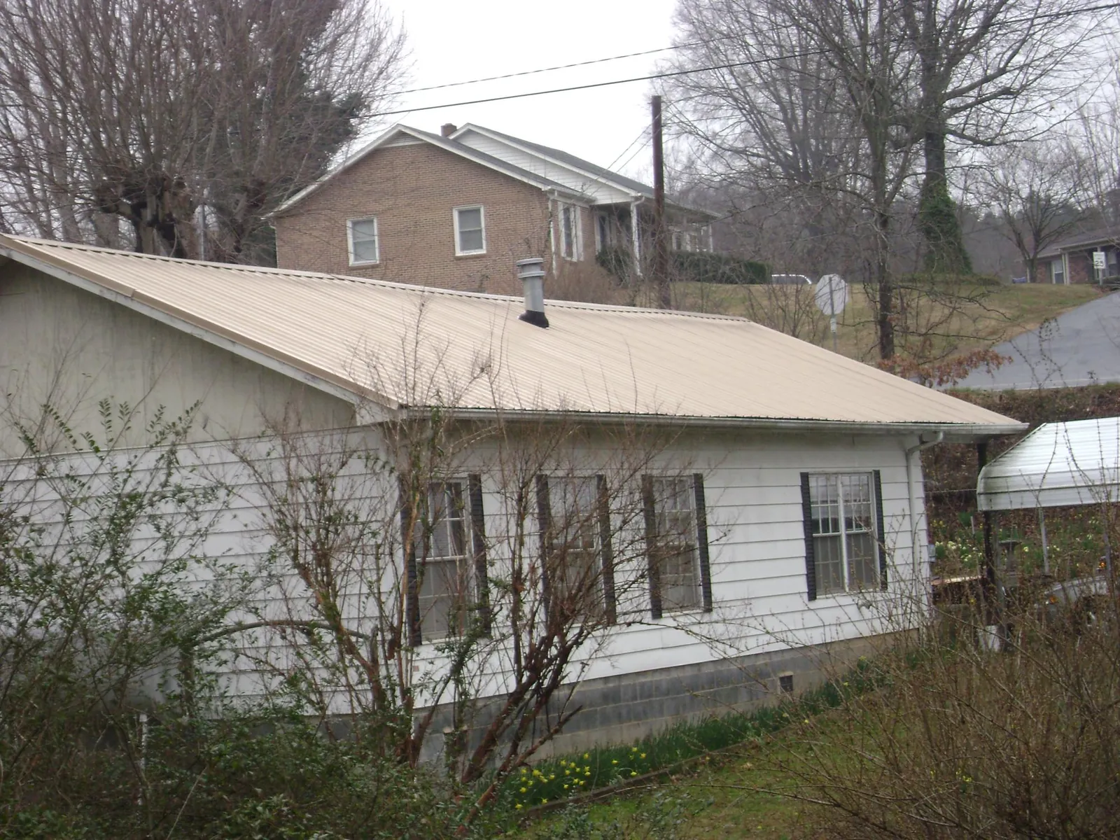 Tan metal roof on a white sided house set into a hillside — Commercial Roofing by Roofing Brothers in Purcellville